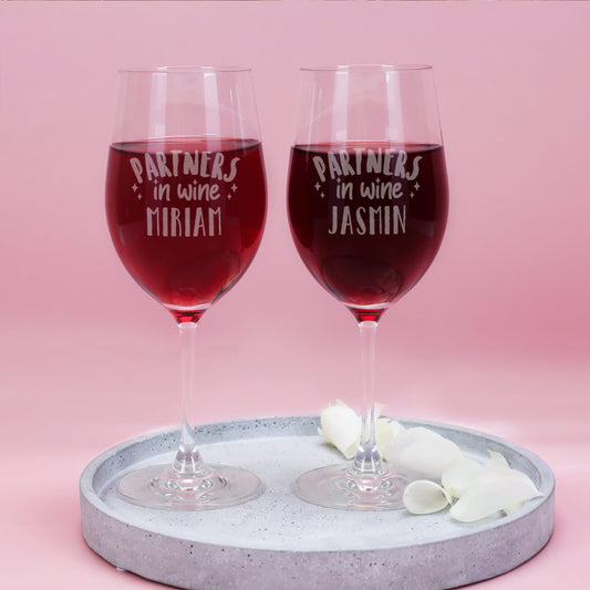 Zwei gravierte Weingläser mit der Aufschrift „Partners in Wine“ und den Namen Miriam und Jasmin, gefüllt mit Rotwein