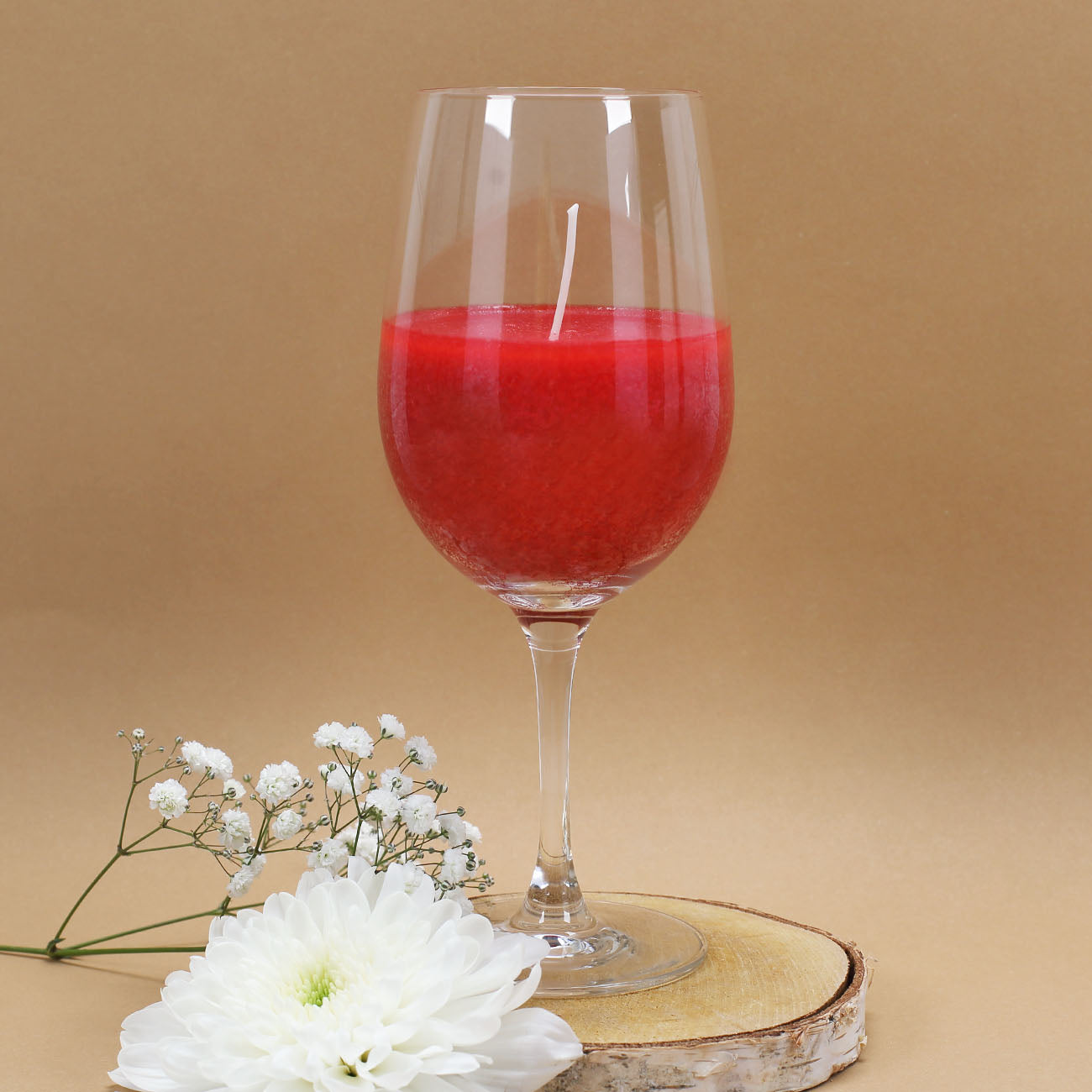 Rote Duftkerze im eleganten Leonardo-Weinglas auf braunem Hintergrund - dekoriert mit weißen Blumen und einer Baumscheibe
