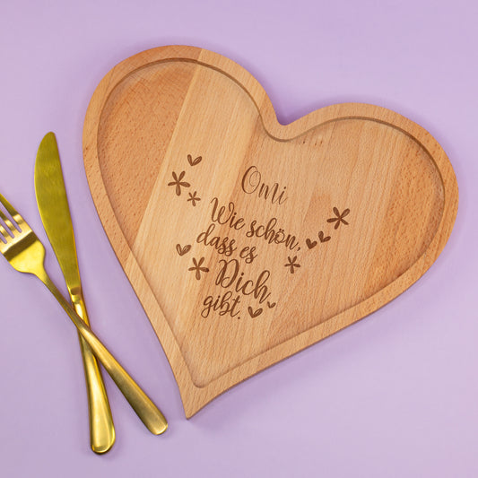 Personalisiertes Herzbrettchen aus Holz mit Gravur „Omi – Wie schön, dass es dich gibt“ auf lila Hintergrund mit Besteck