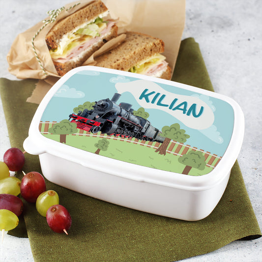 Brotdose mit Eisenbahnmotiv und dem Namen „Kilian“ auf dem Deckel, daneben Sandwiches und Trauben als Schulpausen-Snack.
