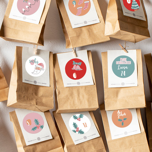 Detailansicht von Adventskalender-Tüten mit rosa und roten Aufklebern, nummeriert von 1 bis 24