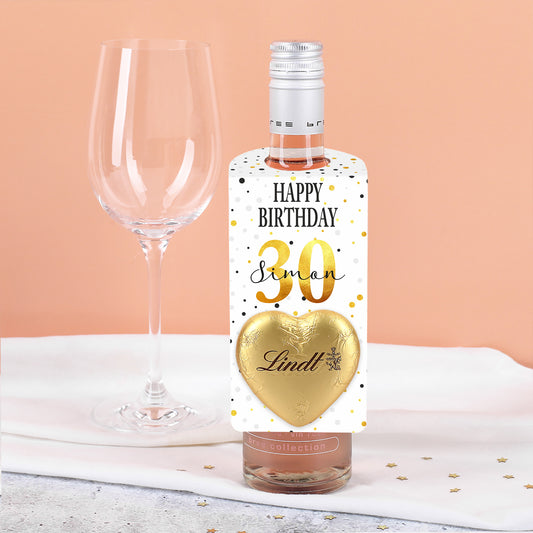 Personalisierter Flaschenanhänger in kleiner Ausführung mit Konfetti-Motiv, goldenem Lindt-Schokoladenherz, Name und Alter – an einer Weinflasche befestigt.