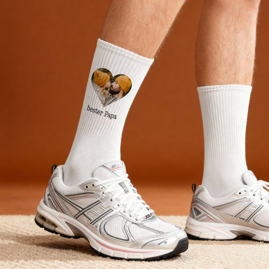 Weiße Foto-Socken mit Herzfoto und Text „bester Papa“, getragen am Fuß vor orangem Hintergrund