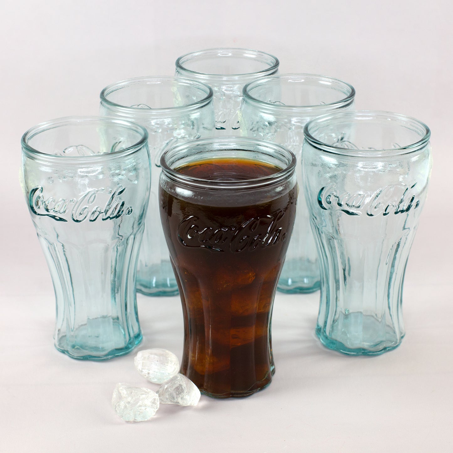Coca-Cola Gläser Set mit fünf leeren Gläsern und einem gefüllten Glas mit Cola und Eiswürfeln