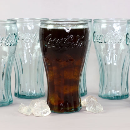 Retro Coca-Cola Trinkglas mit Cola und Eiswürfeln vor mehreren Gläsern aus recyceltem Glas