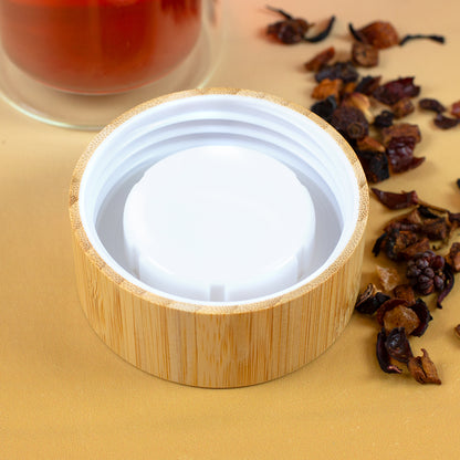 Innenseite des Bambusdeckels mit weißem Schraubverschluss neben losem Früchtetee und Glasflasche