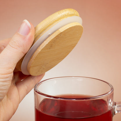 Bambusdeckel wird von Hand von der Glastasse mit rotem Tee abgenommen