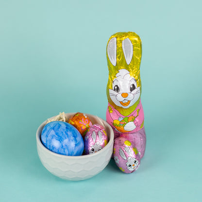 Riegelein Oster-Mischbeutel 100g ausgepackt stehend neben einem grauen Becher aus Keramik mit Holzwolle