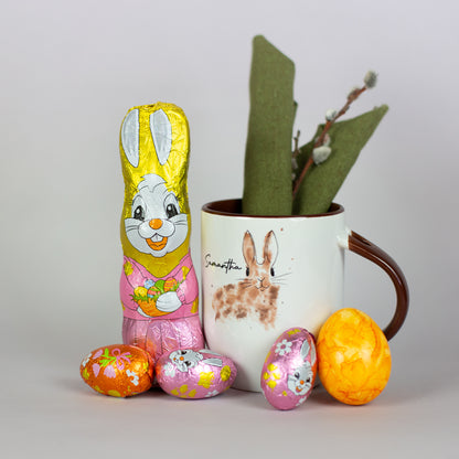 Riegelein Oster-Mischbeutel 100g ausgepackt stehend neben einer Tasse mit Oster-Motiv