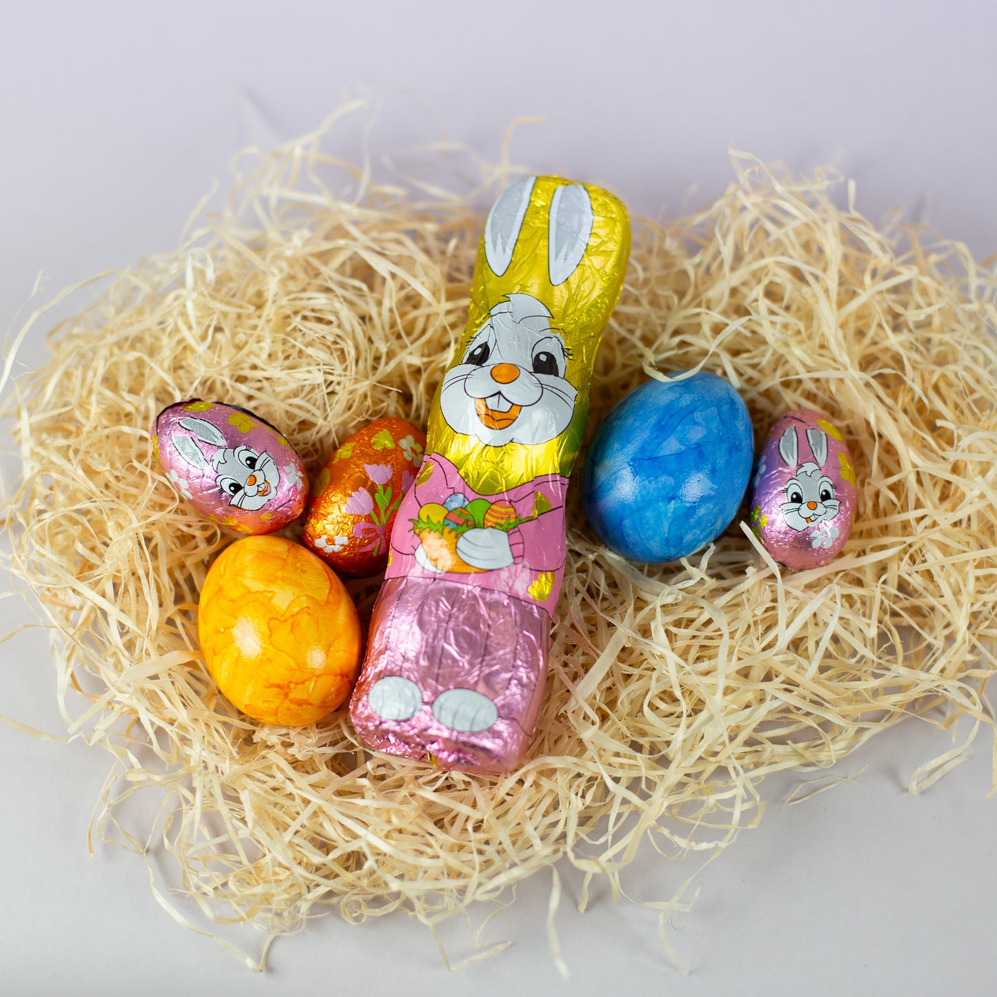 Riegelein Oster-Mischbeutel 100g ausgepackt liegend auf ausgebreiteter Holzwolle zusammen mit zwei gefärbten Eiern