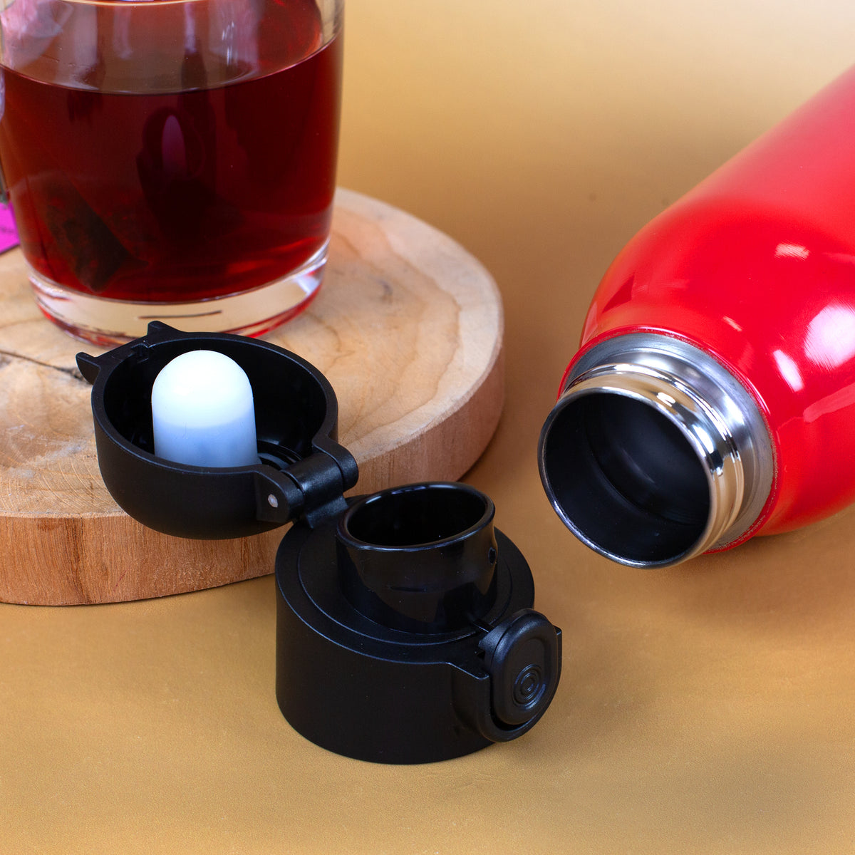 Rote Edelstahl-Trinkflasche mit abgeschraubtem Klickdeckel und sichtbarer Flaschenöffnung neben einem Glas Tee