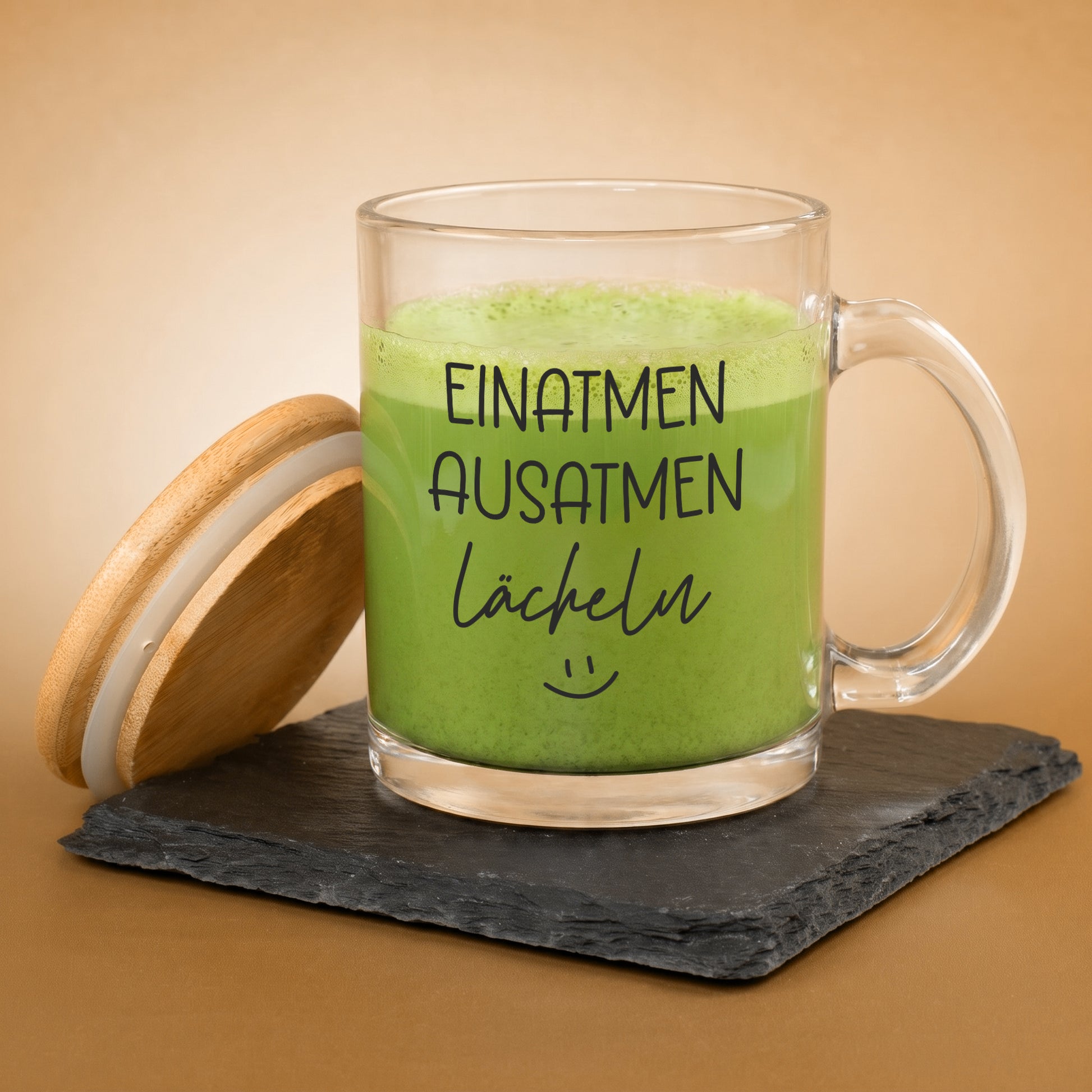 Glastasse mit grünem Matcha, Bambusdeckel und Aufdruck Einatmen Ausatmen Lächeln