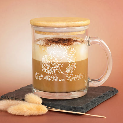 Glastasse mit Cappuccino, Bambusdeckel und „Komme was Wolle“ Motiv auf schwarzer Schieferplatte