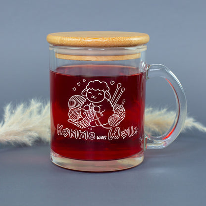 Glastasse mit rotem Tee, Bambusdeckel und weißem Strickmotiv mit Schaf, Wolle und Stricknadeln