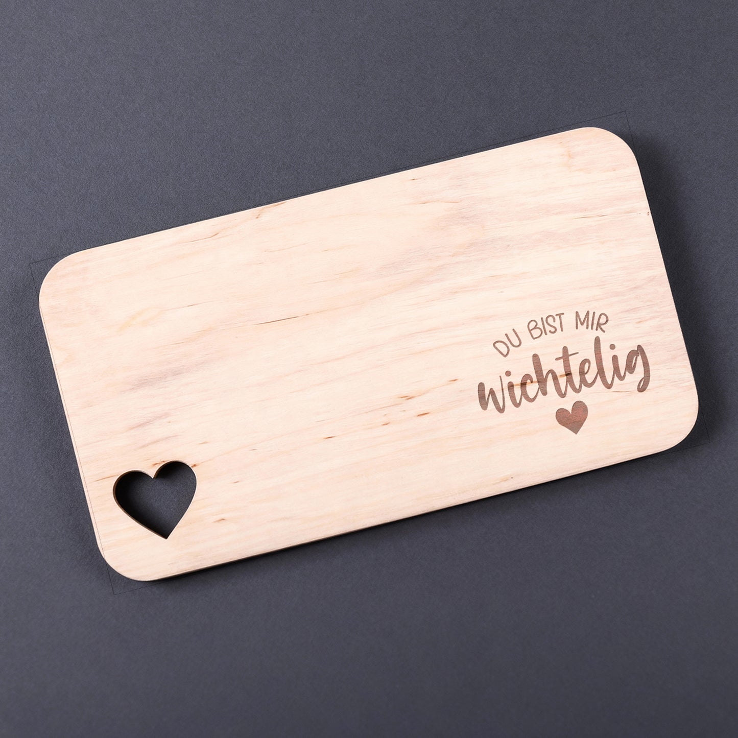 Holzbrettchen mit Spruch „Du bist mir wichtelig“ und Herzmotiv vor dunklem Hintergrund.