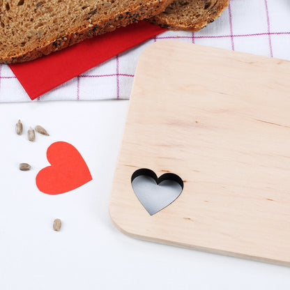 Detailaufnahme des Herzausschnitts im Holzbrettchen, umgeben von Brot und Deko.