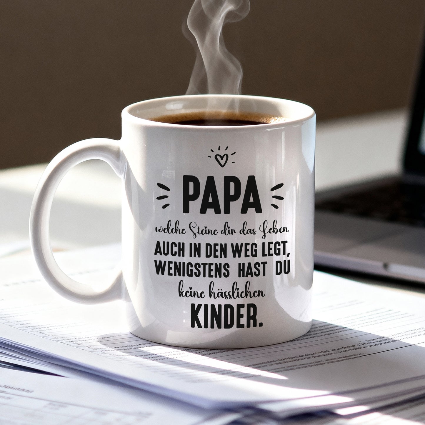 Witzige Tasse für Papa mit Spruch „wenigstens hast du keine hässlichen Kinder“, steht dampfend neben Laptop
