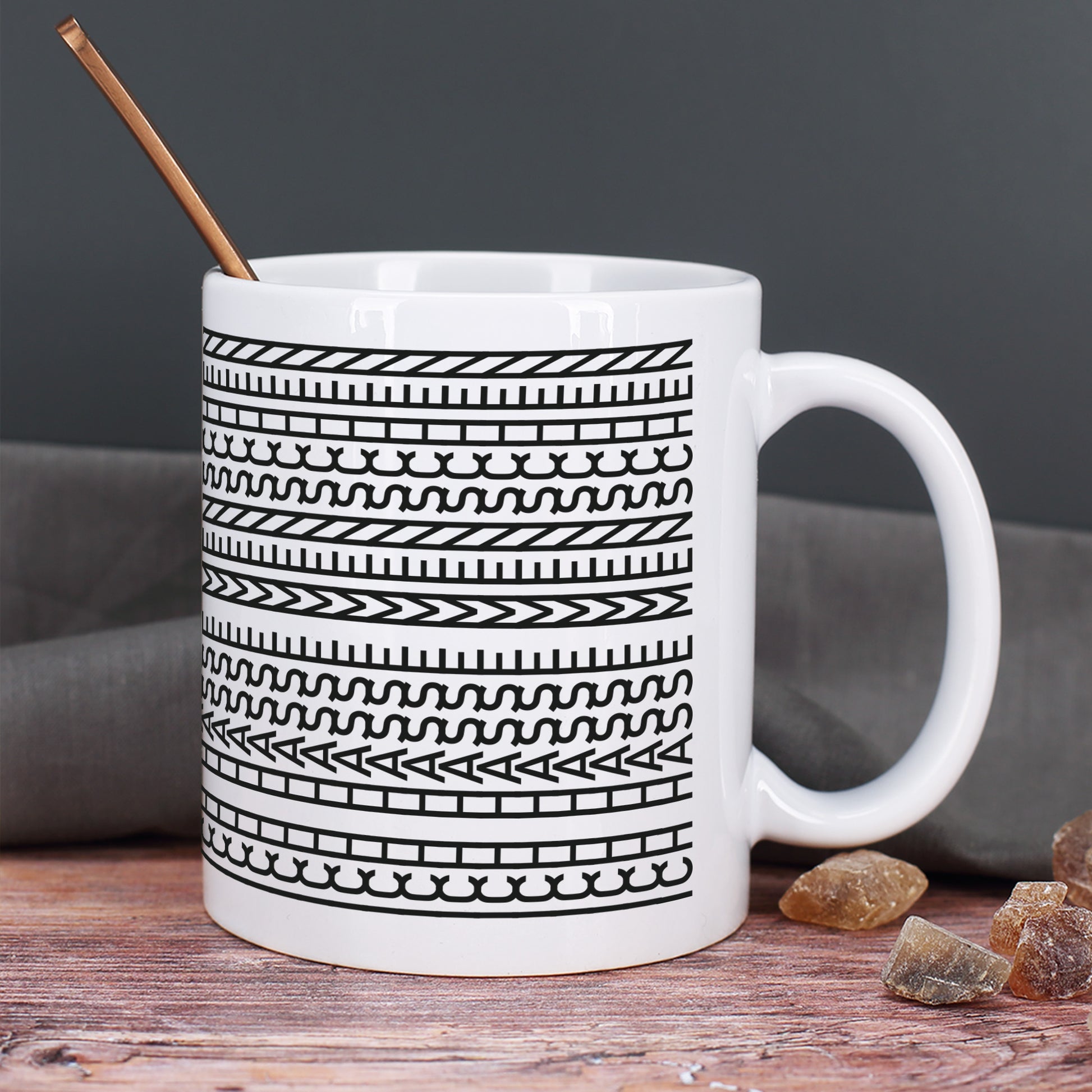 Keramiktasse mit Schwarz-Weiß-Muster und Löffel auf Holztisch mit dunklem Hintergrund