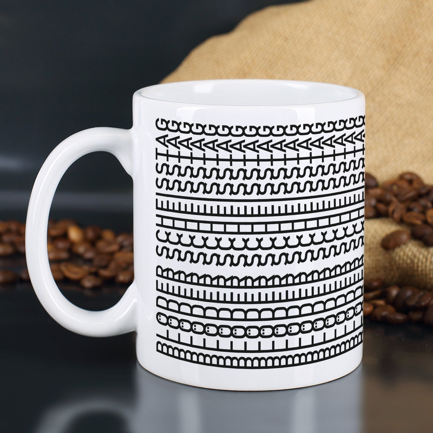 Kaffeetasse mit schwarzem Musterdruck und versteckter Botschaft „Blöder Scheißtag“ vor Kaffeesack und Kaffeebohnen