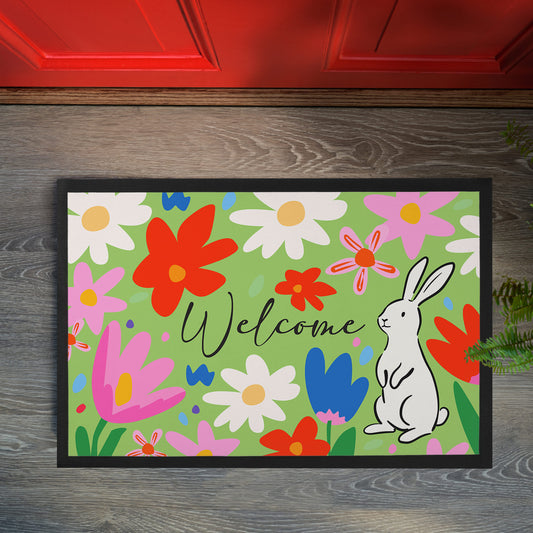 Frühlings Fußmatte mit Blumenwiese Design und weißem Hasen neben Welcome Schriftzug vor einer Haustür