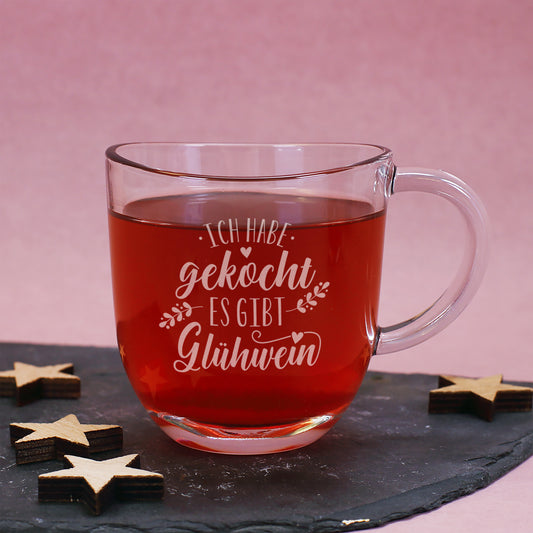 Glühweintasse aus Glas mit Gravur und rotem Glühwein auf Schieferplatte mit Holzsternen