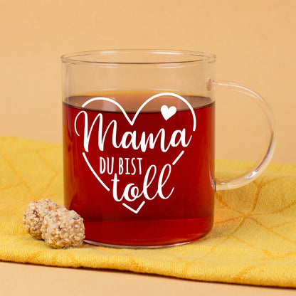 Teeglas mit Aufdruck Mama du bist toll und Herzmotiv auf gelbem Hintergrund mit Gebäck