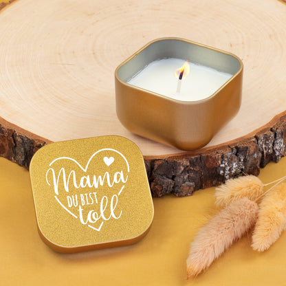 Goldene Duftkerze „Mama du bist toll“ geöffnet mit brennender Flamme auf Holzscheibe