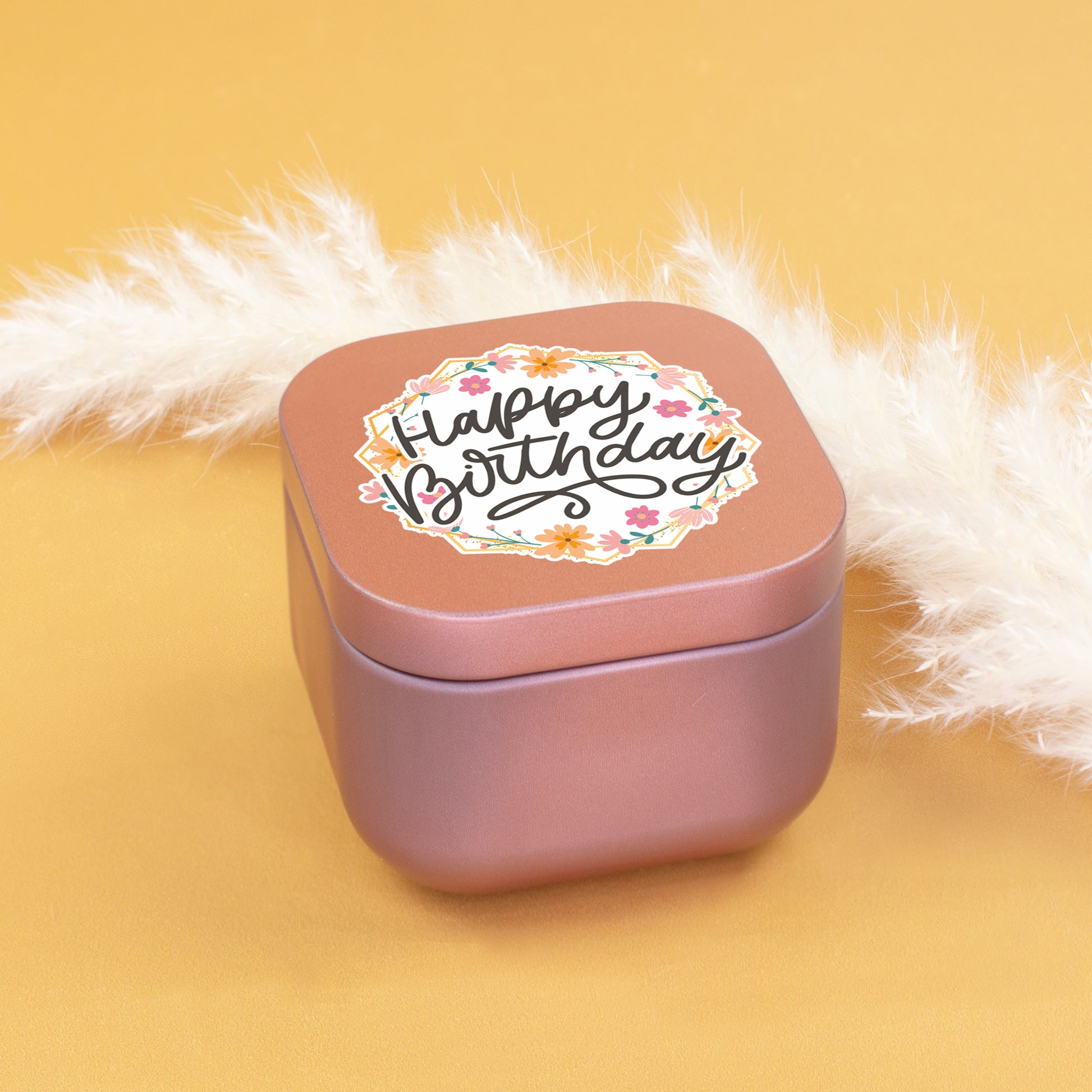 Geschlossene roségoldene Duftkerze mit Happy Birthday Aufdruck vor hellem Hintergrund