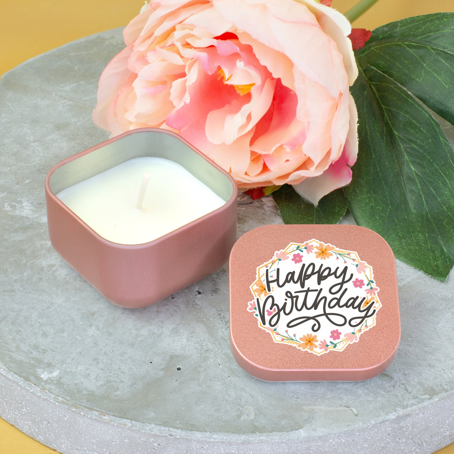 Roségoldene Mini Duftkerze mit Happy Birthday Deckel neben großer Blume dekoriert