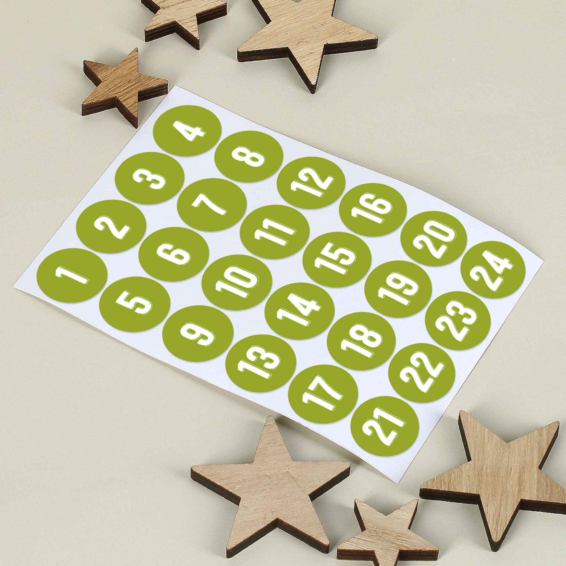 Bogen mit 24 nummerierten Aufklebern in Grün, daneben kleine Holzsterne auf hellem Hintergrund