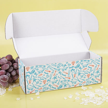 Geöffnete Geschenkbox mit farbigem Werkzeug-Muster und Deko auf gelbem Hintergrund mit WeintraubenDeko.