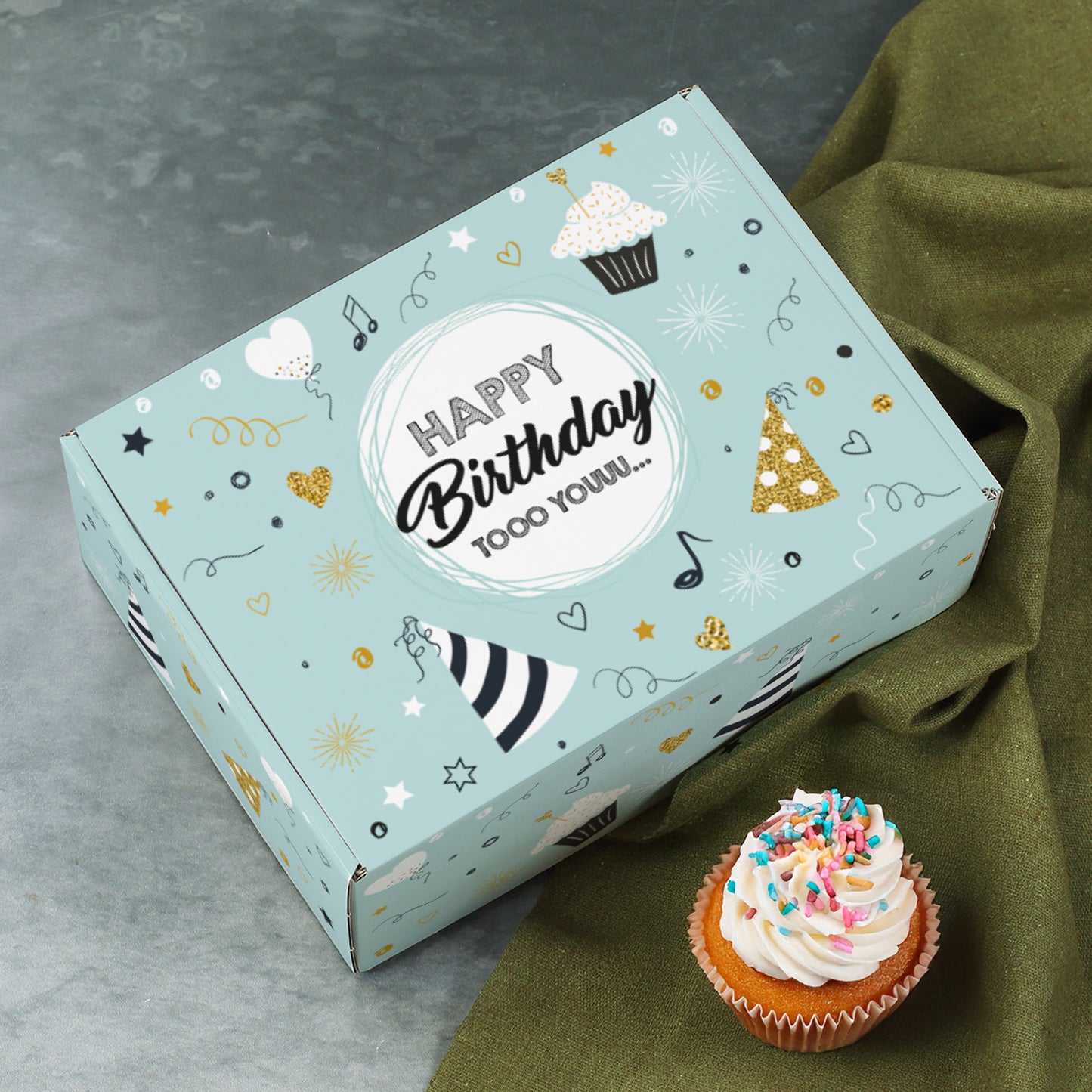 Geschlossene Geschenkbox auf grauem Untergrund mit Cupcake, Motiv „Happy Birthday tooo youuu…“ in der Mitte