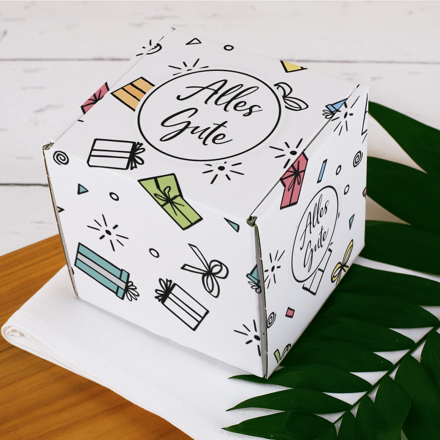 Quadratische Geschenkbox „Alles Gute“ in Nahaufnahme, zeigt die detailreiche, bunte Geschenkverpackung mit Rundumdruck.