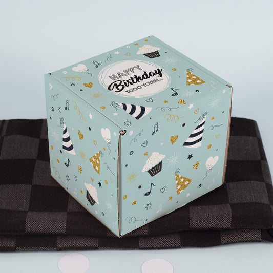 Geschlossene Geschenkbox mit Spruch „Happy Birthday tooo youuu…“ auf kariertem Stoff