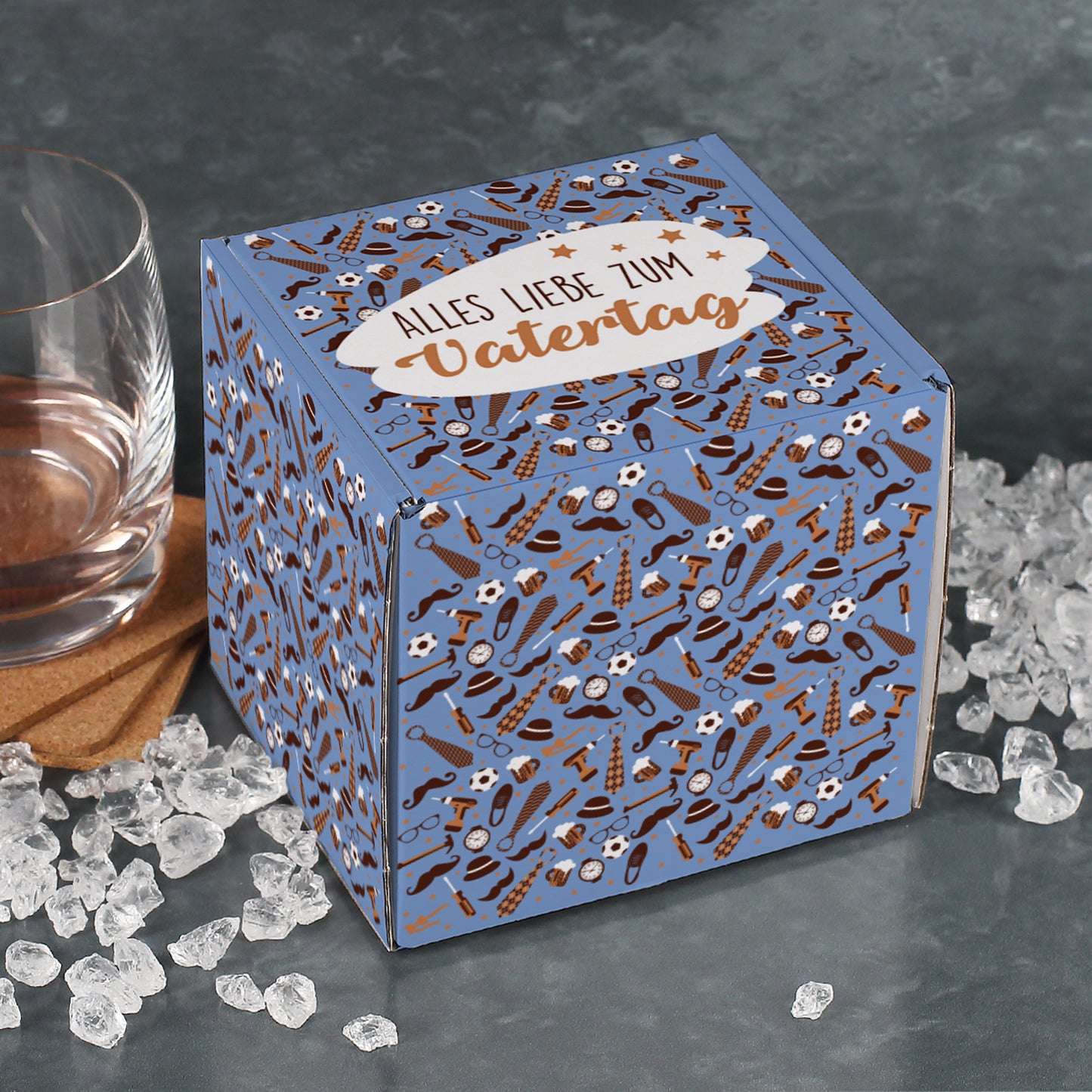 Quadratische Vatertagsbox mit Aufdruck „Alles Liebe zum Vatertag“, dekorativ platziert auf grauem Untergrund mit Glas