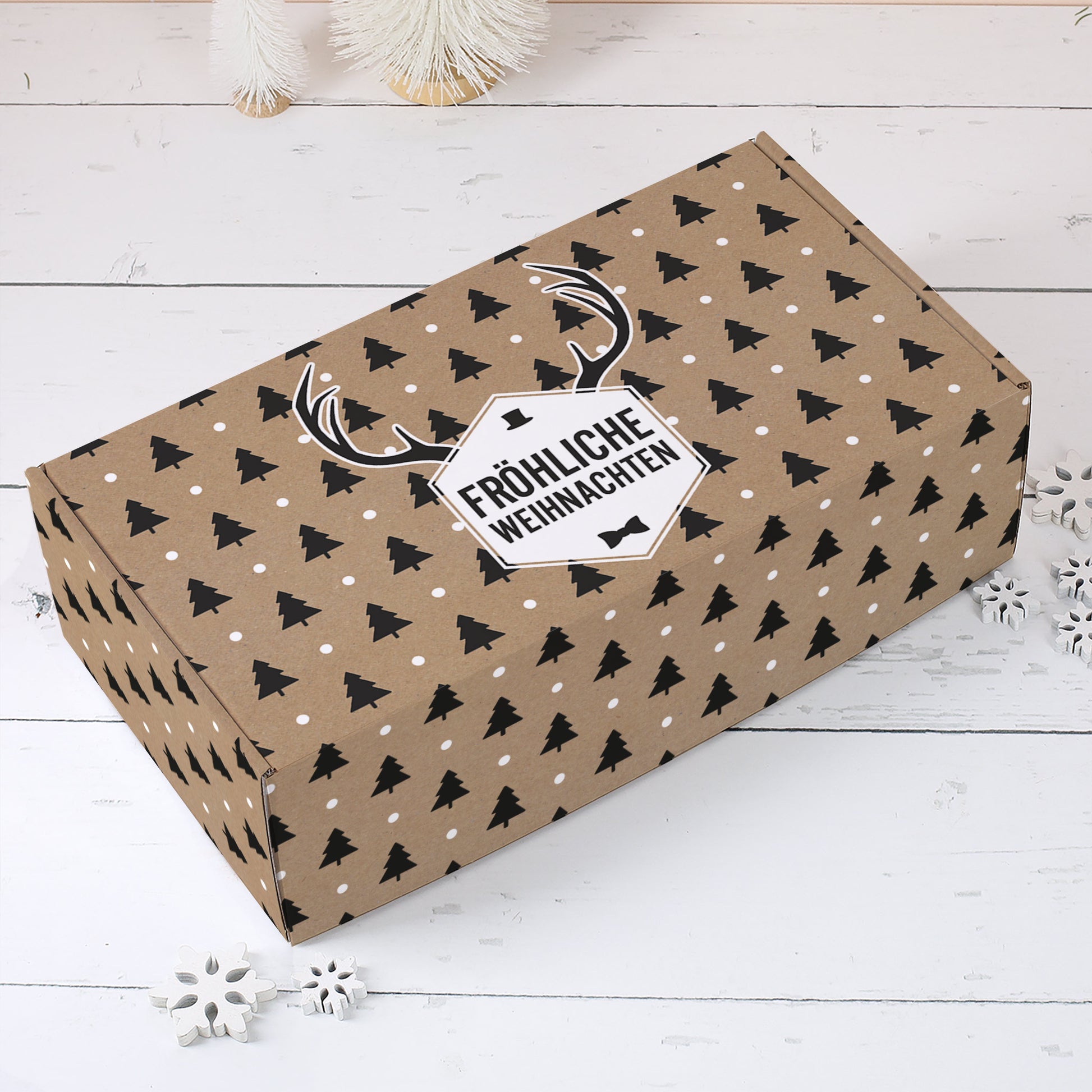 Braune Geschenkbox zu Weihnachten mit schwarzen Tannen, weißen Punkten, Rentiergeweih und Fröhliche Weihnachten Etikett