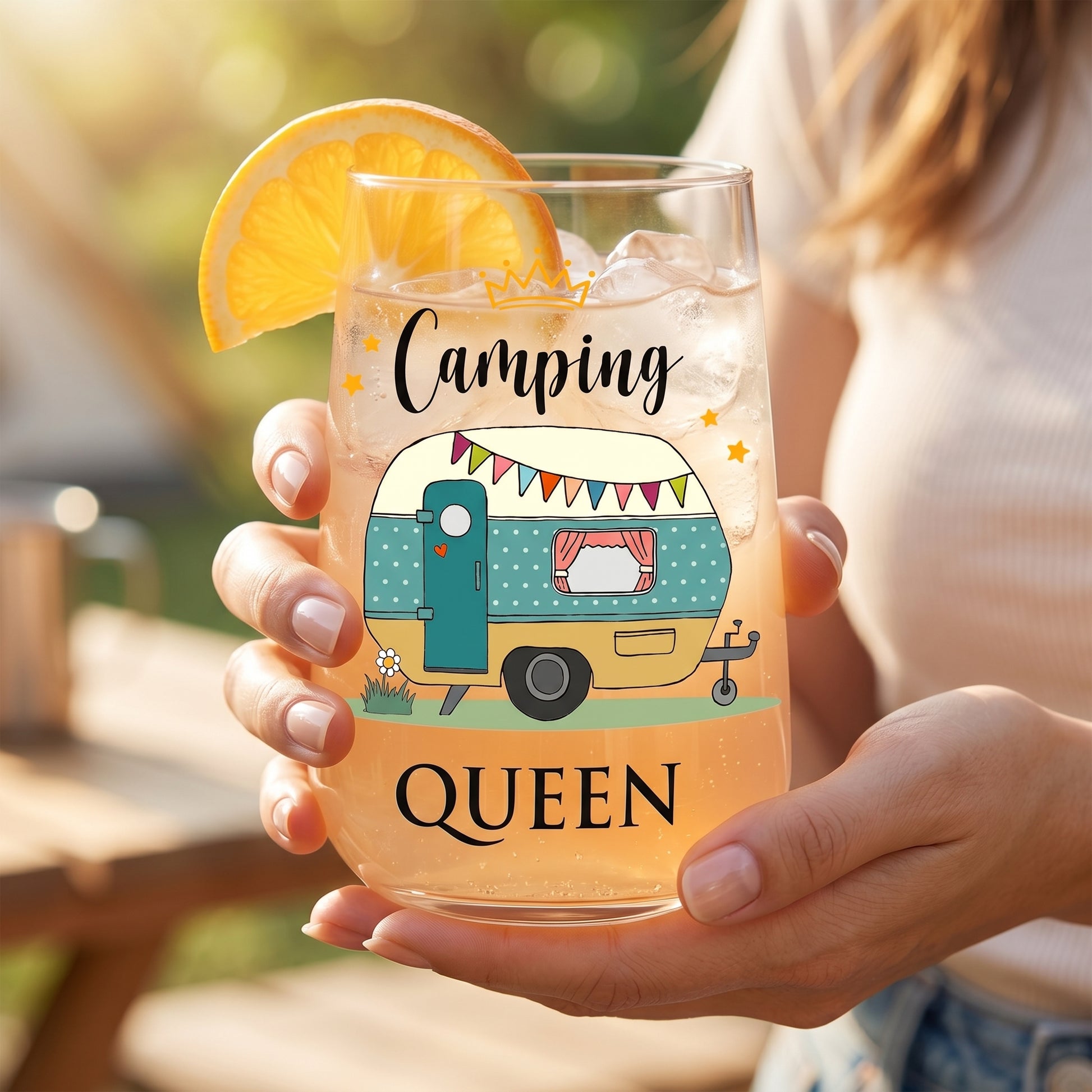 Trinkglas Camping Queen mit Wohnwagen-Motiv, Orangenscheibe und hellem Sommerdrink in der Hand