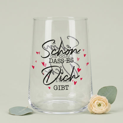 Leeres Trinkglas mit Aufdruck Schön dass es Dich gibt und roten Herzen neben Blume und Eukalyptus