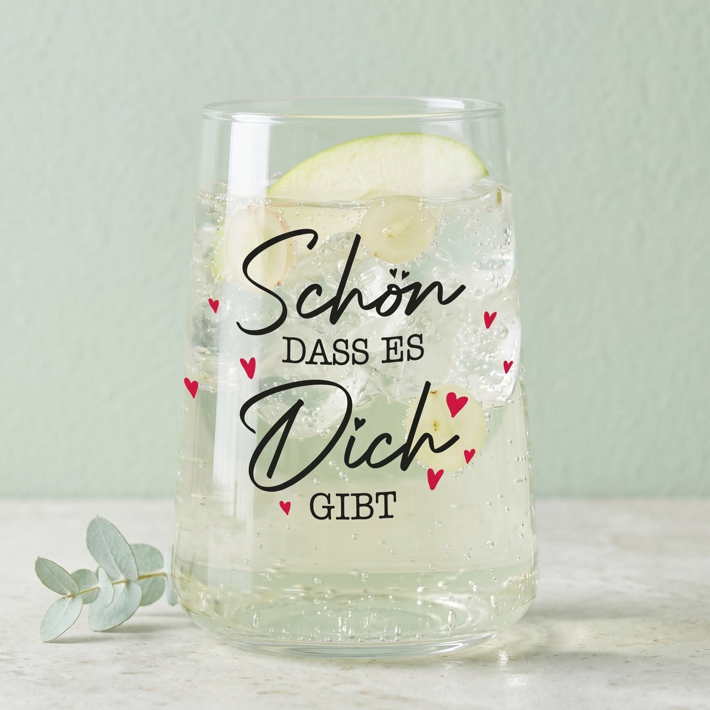 Trinkglas mit Aufdruck Schön dass es Dich gibt, gefüllt mit hellem Getränk und grüner Dekoration