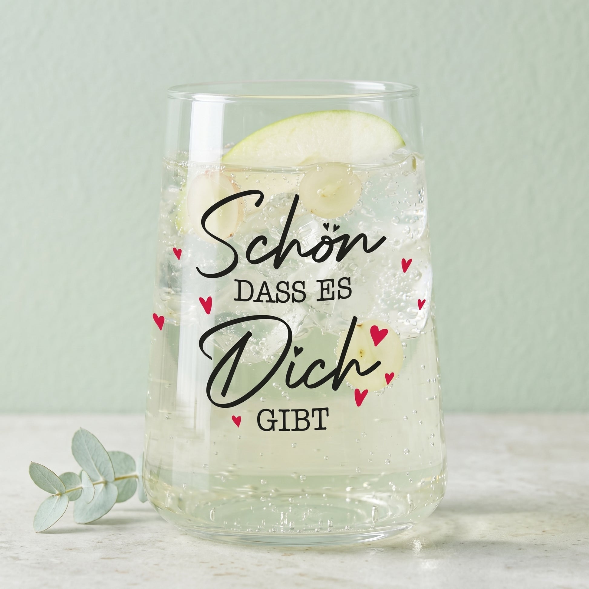Trinkglas mit Aufdruck Schön dass es Dich gibt, gefüllt mit hellem Getränk und grüner Dekoration