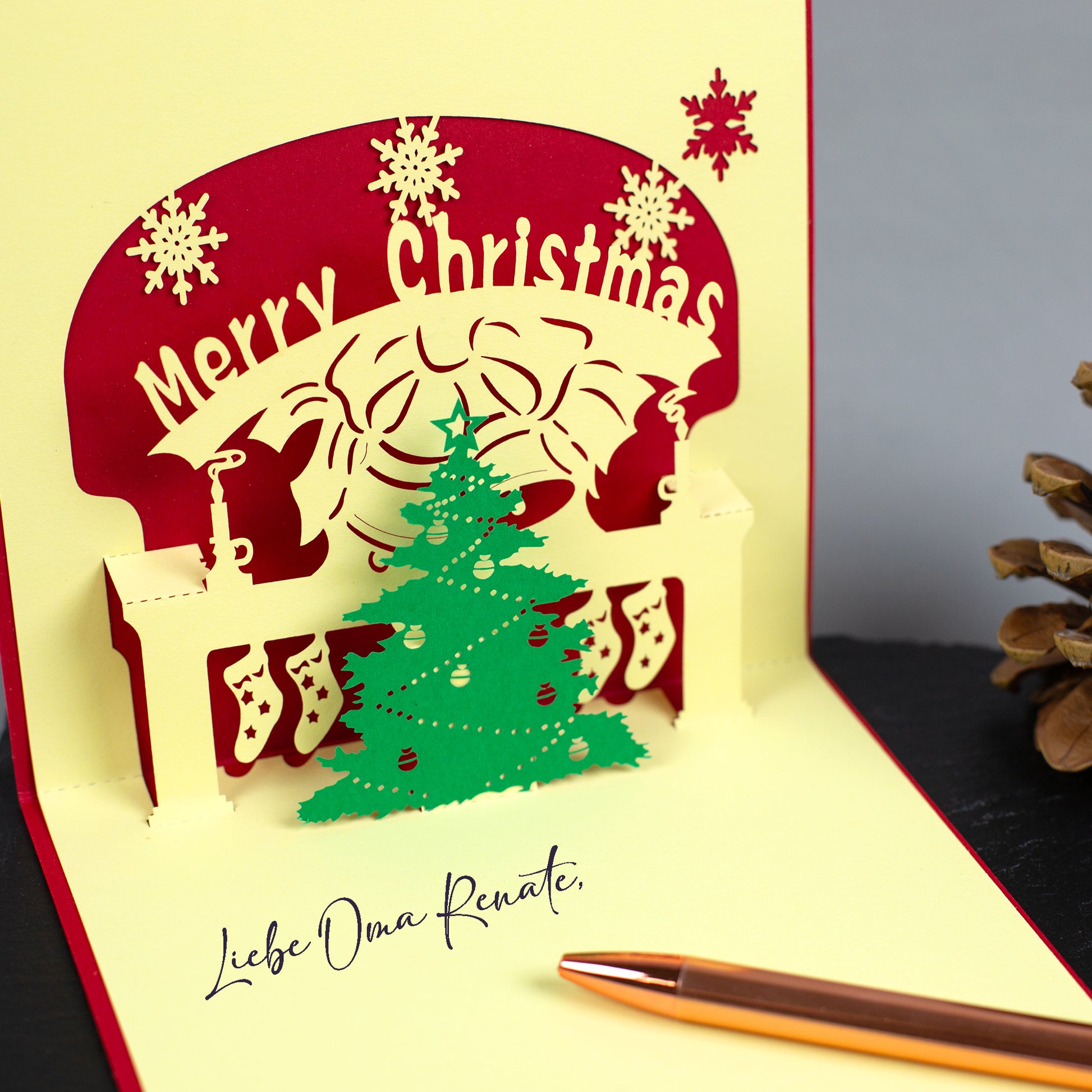 Innenansicht einer 3D-Karte mit Kamin, Weihnachtsbaum und Scherenschnitt-Dekor, Text „Merry Christmas“ sichtbar.