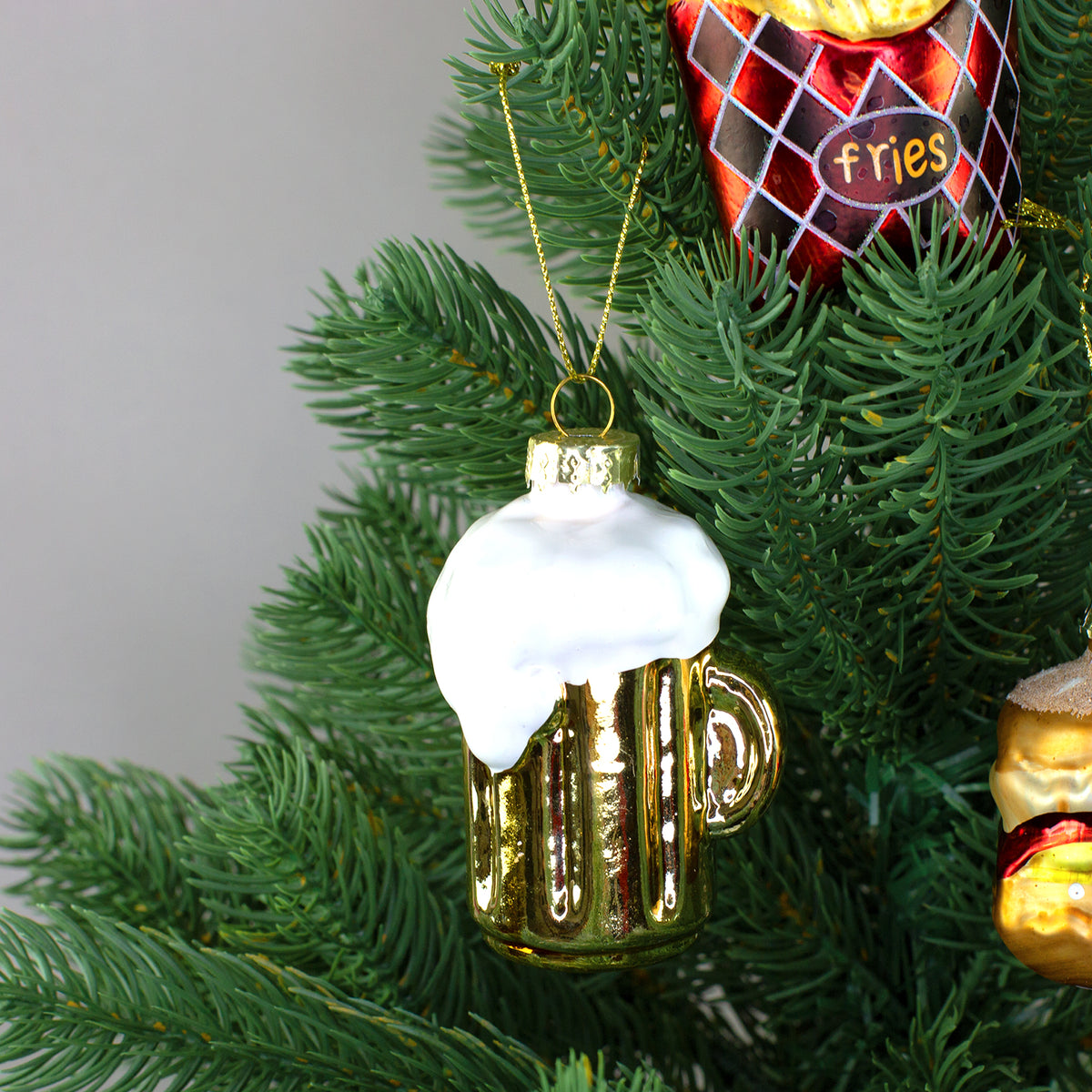 Goldfarbener Bierkrug mit weißem Schaum als Glas-Baumschmuck am Tannenbaum