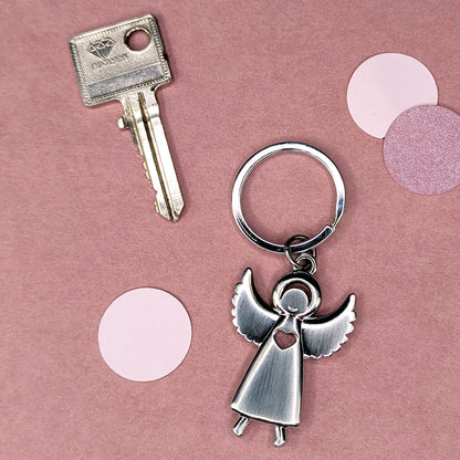Schlüsselanhänger in Engel-Form neben einem Schlüssel, von oben fotografiert auf rosafarbenem Hintergrund