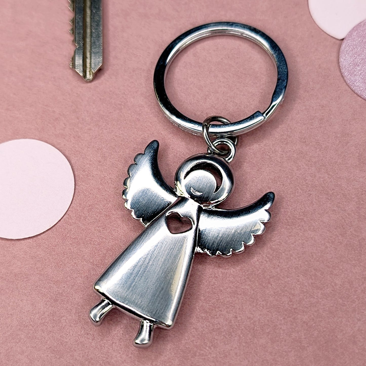 Metall-Engel-Schlüsselanhänger in schräger Perspektive mit sichtbarer Herzöffnung, auf rosa Hintergrund