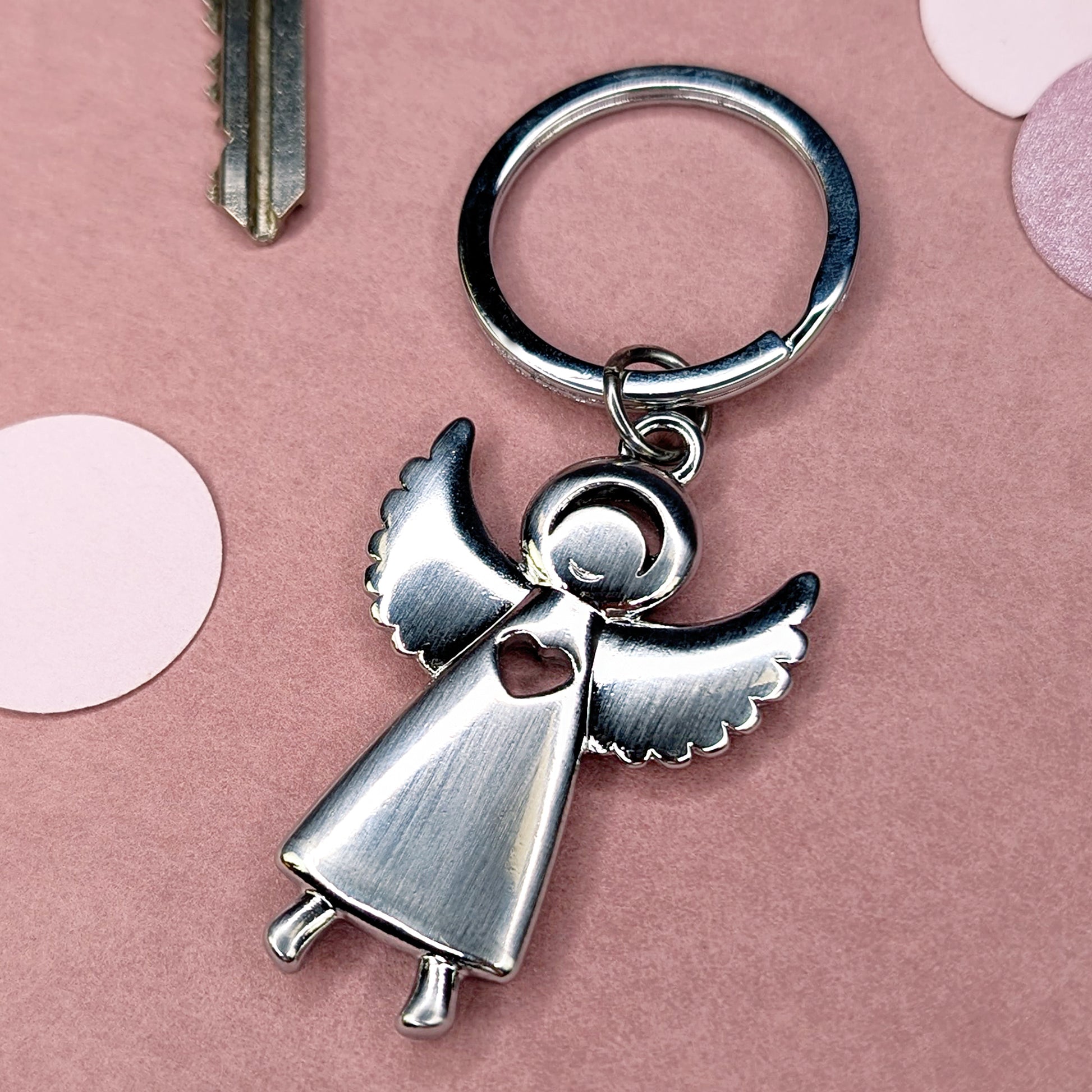 Metall-Engel-Schlüsselanhänger in schräger Perspektive mit sichtbarer Herzöffnung, auf rosa Hintergrund