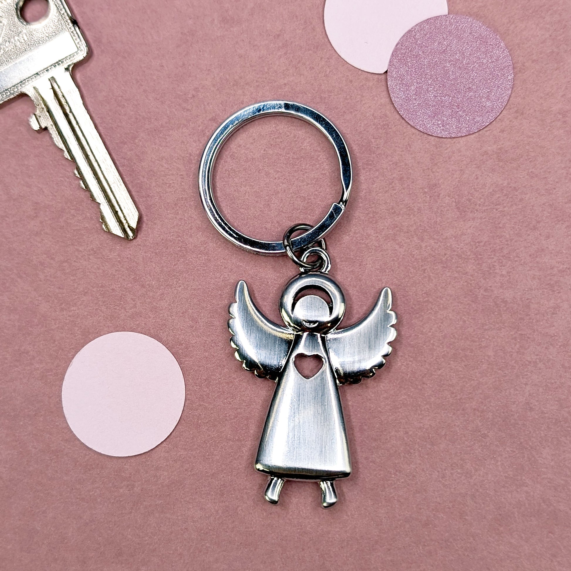 Flacher Schlüsselanhänger in Form eines Engels mit ausgestreckten Flügeln, liegend neben einem Schlüssel
