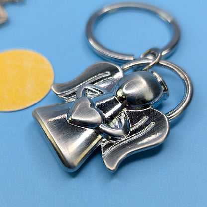 Nahaufnahme des Engelschlüsselanhängers mit herzförmigem Detail, silberfarben, auf blauem Untergrund