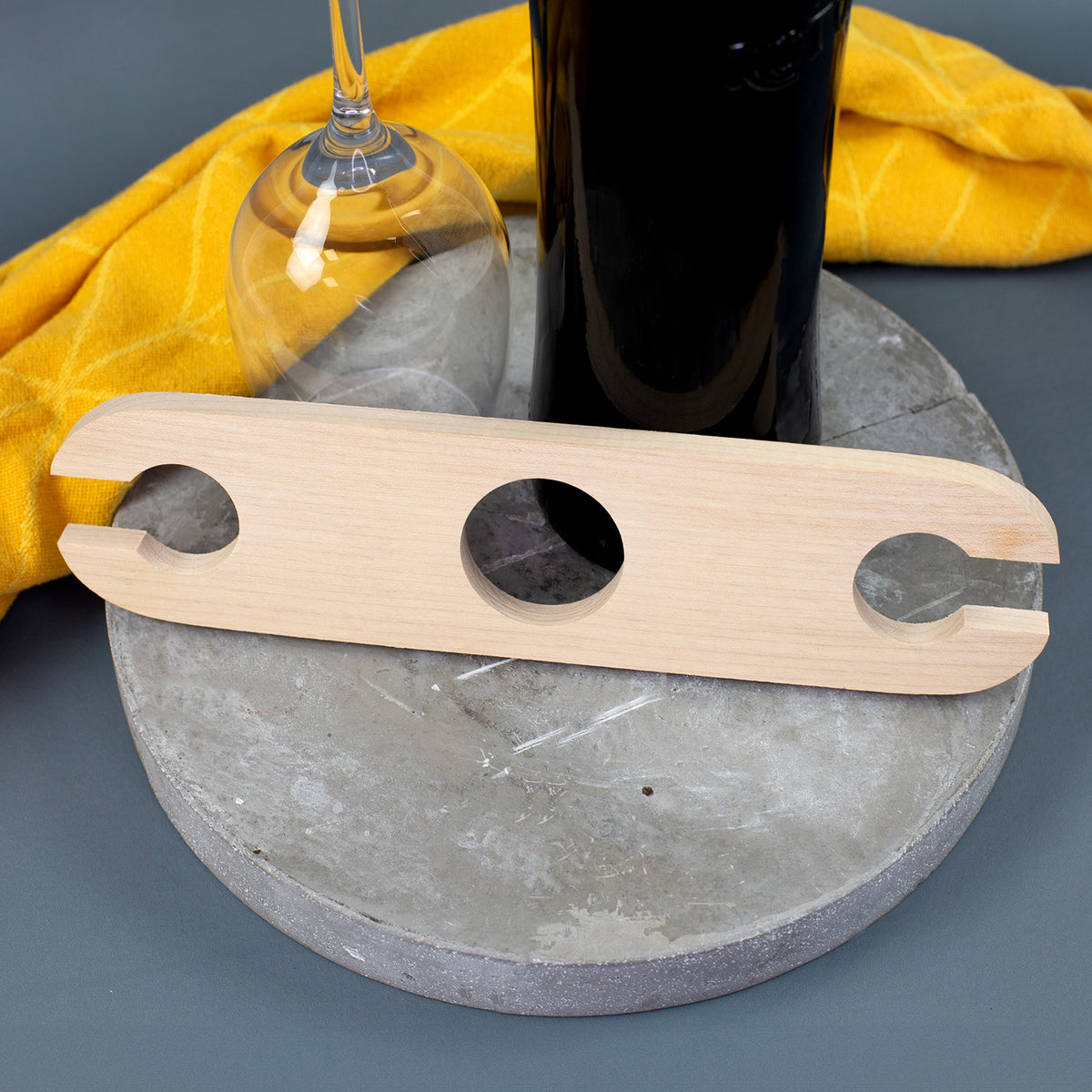 Weinbutler aus hellem Holz mit drei Aussparungen für eine Weinflasche und zwei Weingläser auf grauer Ablage
