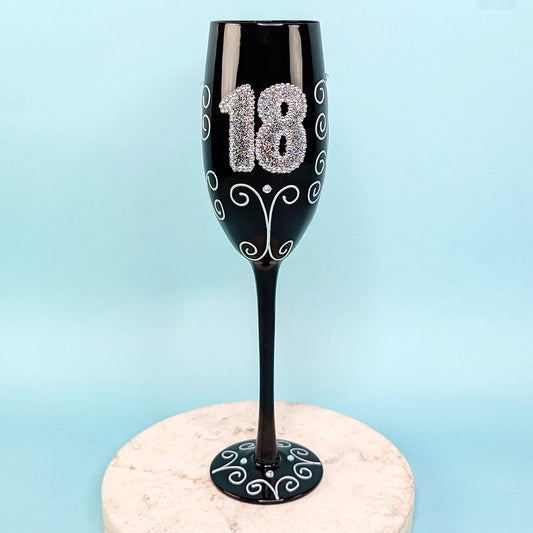 Schwarzes Sektglas mit glitzernder 18 und Ornamenten, frontal fotografiert