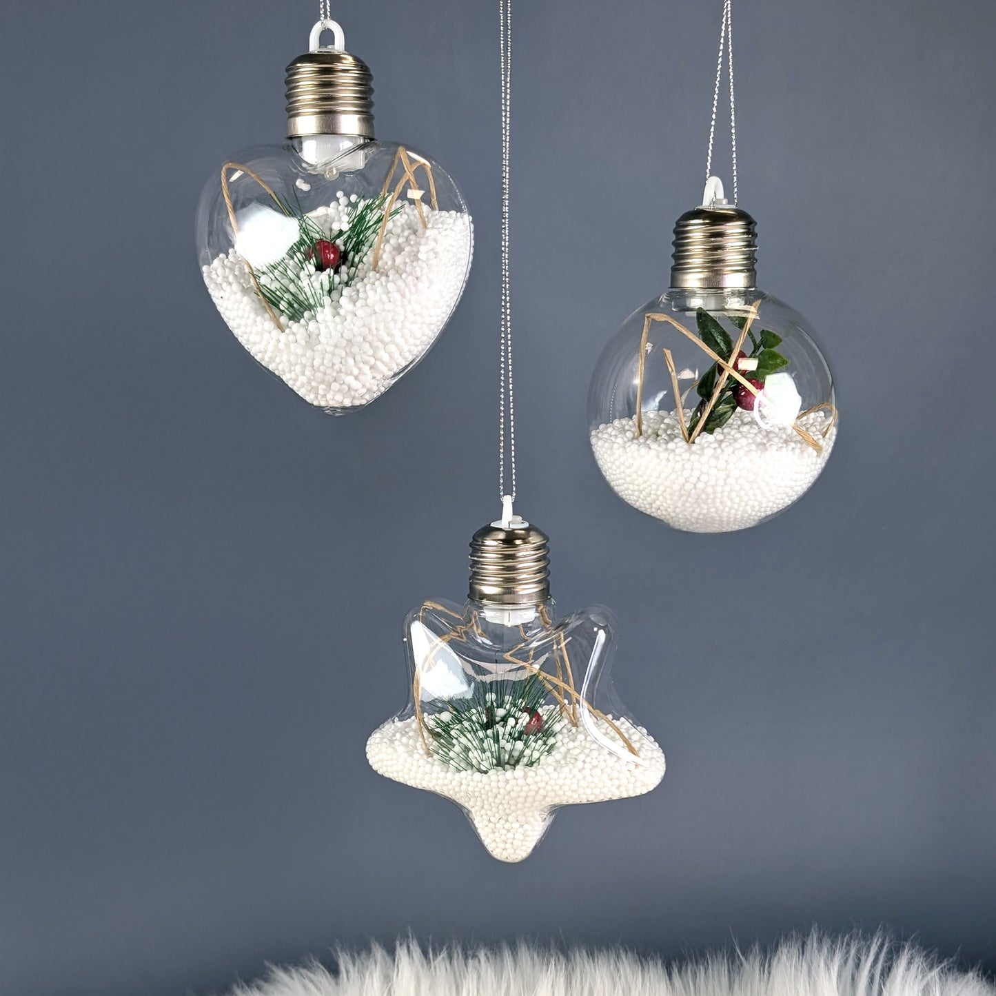 Drei beleuchtete Christbaumkugeln mit Styroporkugeln, Zweigen und roten Beeren vor grauem Hintergrund.